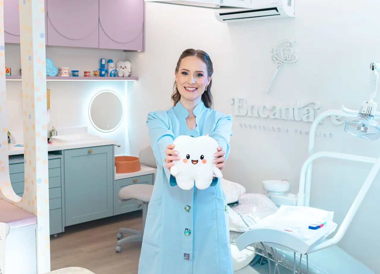 Dra. Daphynne, odontopediatra da Encantare, segurando um dente de pelúcia no consultório infantil em Curitiba